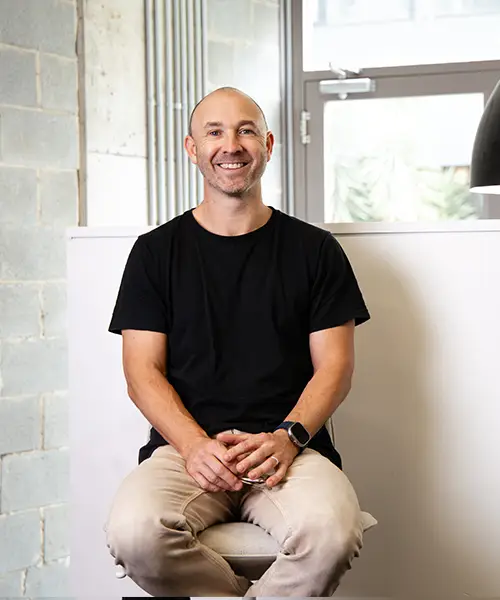 Andrew, sports Podiatrist, sits comfortably on a chair with a welcoming smile