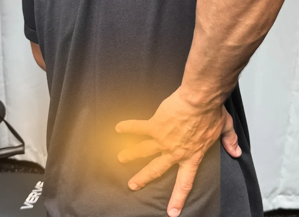 Person from behind touching their lower back, highlighted with an orange glow to indicate Lower Back Pain