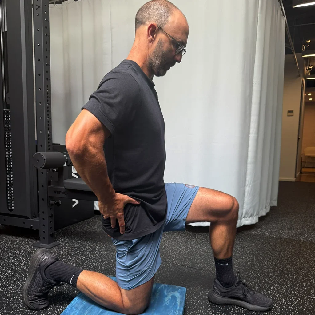Person kneeling on a blue mat, in a lunge position, performing a hip flexor stretch