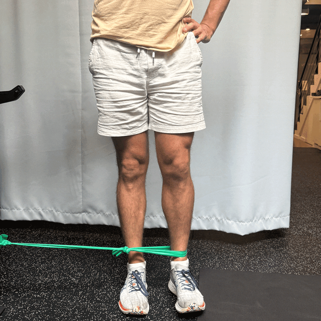 Person standing and performing a side leg raise exercise, with a green resistance band around their ankles