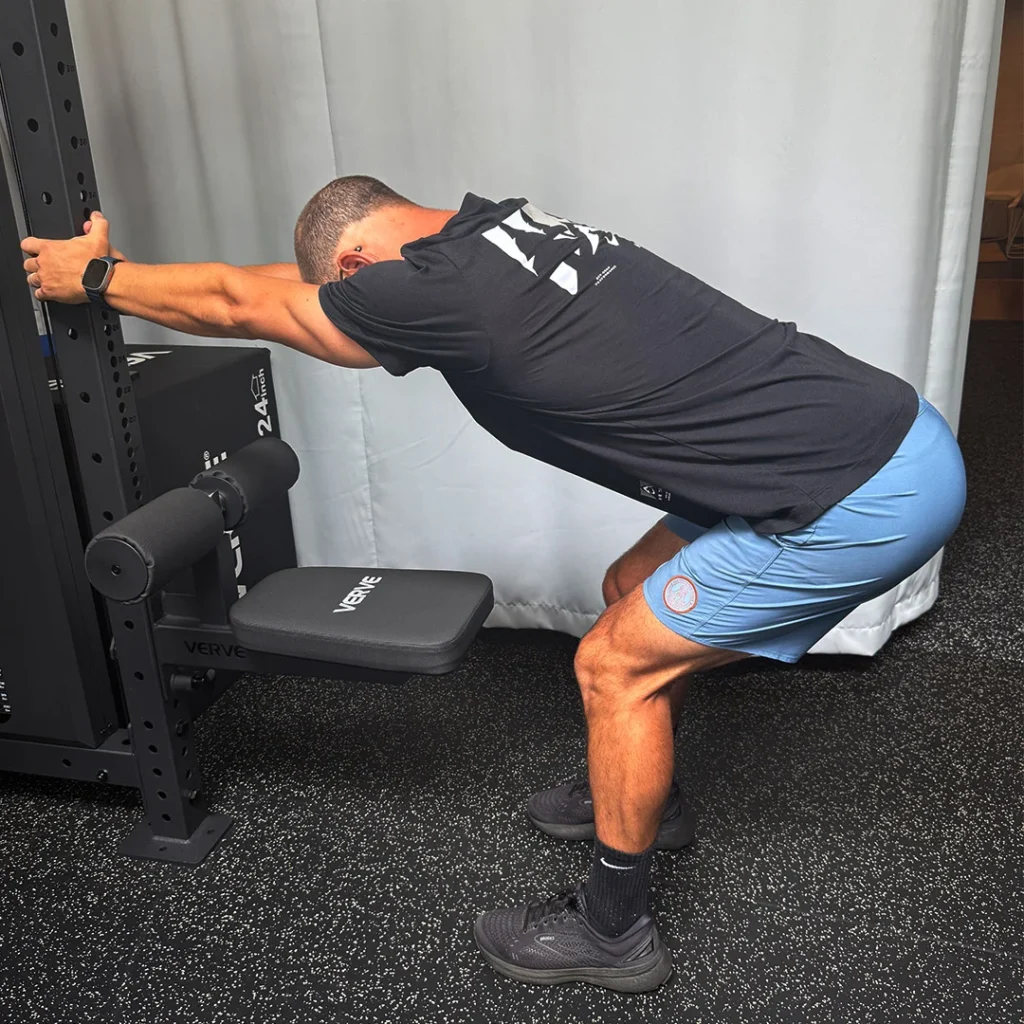 Person standing, performing a hip hinge exercise with a stick, to strengthen their lower back